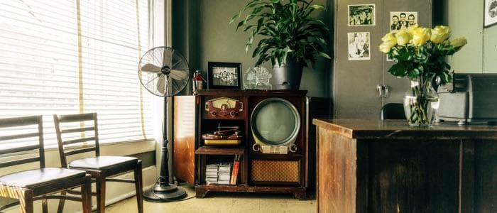  An old office with a dated interior design. Older style television, black and white photos, and an antique fan sit inside the cramped office space. 